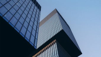 Vue plongeante sur deux bâtiments modernes en verre à l'architecture angulaire devant un ciel bleu limpide.