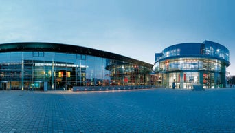 Moderne Glasfassade eines großen Gebäudekomplexes am Abend mit gepflastertem Vorplatz.