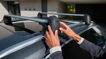 Hände befestigen Dachträger auf grauem Audi vor Wohnhaus.