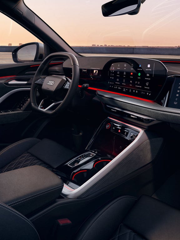 Innenraum eines Audi SQ5 SUV mit roter Ambientebeleuchtung, Sportsitzen und großem Display bei Sonnenuntergang.