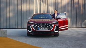 Ein Mann steigt aus einem roten Audi SQ5 vor einer modernen Gebäudefassade mit vertikaler Struktur.