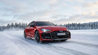Ein roter Audi RS 5 Avant fährt über eine verschneite Straße vor einem verschneiten Wald.