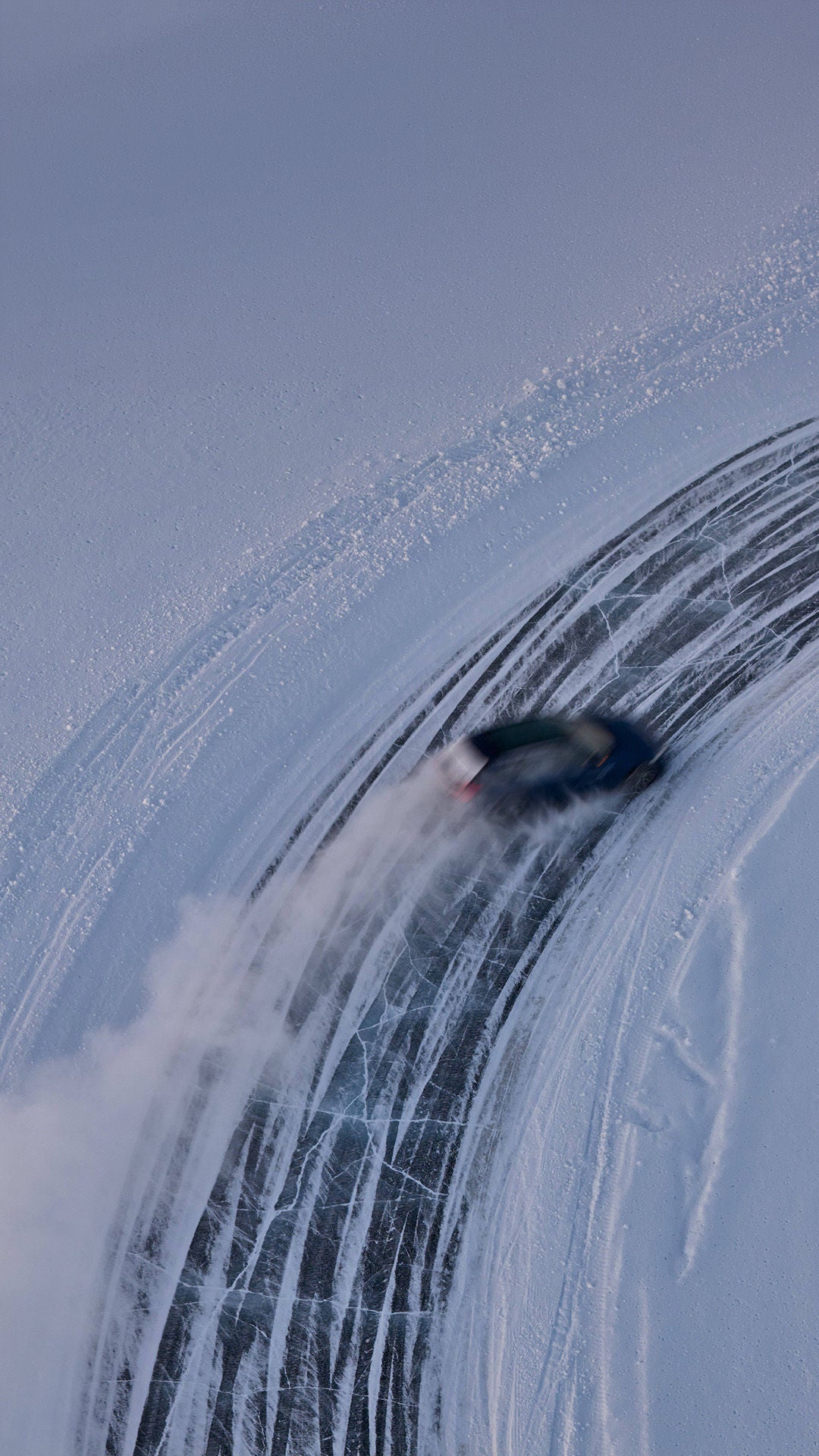 A car drifts on an icy curve; a bird's-eye view of snow spray and tire tracks.