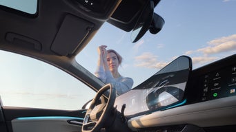 Blick aus dem Innenraum eines Autos auf eine Frau vor der Tür, moderner Innenraum und heller Himmel im Hintergrund.