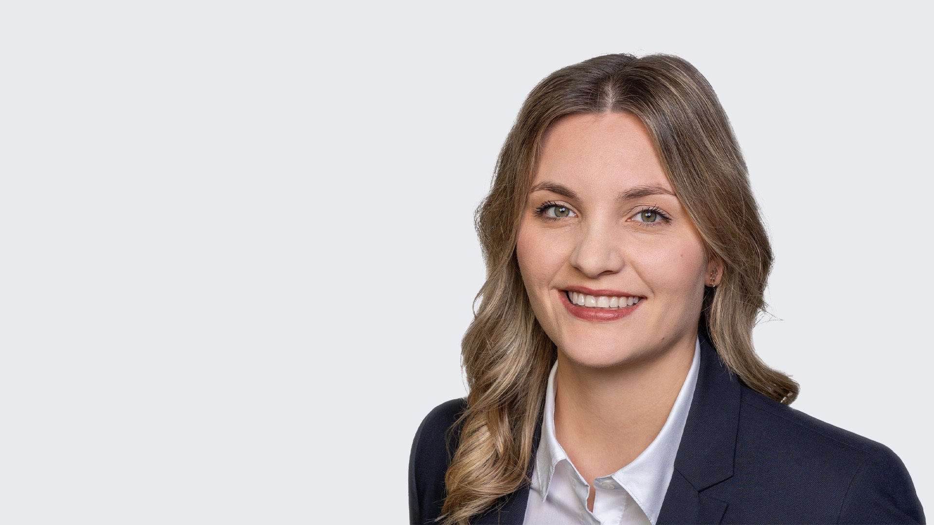 Viktoria Faust: Porträt einer jungen, lächelnden Frau mit blonden, gewellten Haaren, weißer Bluse und dunklem Blazer vor grauem Hintergrund.