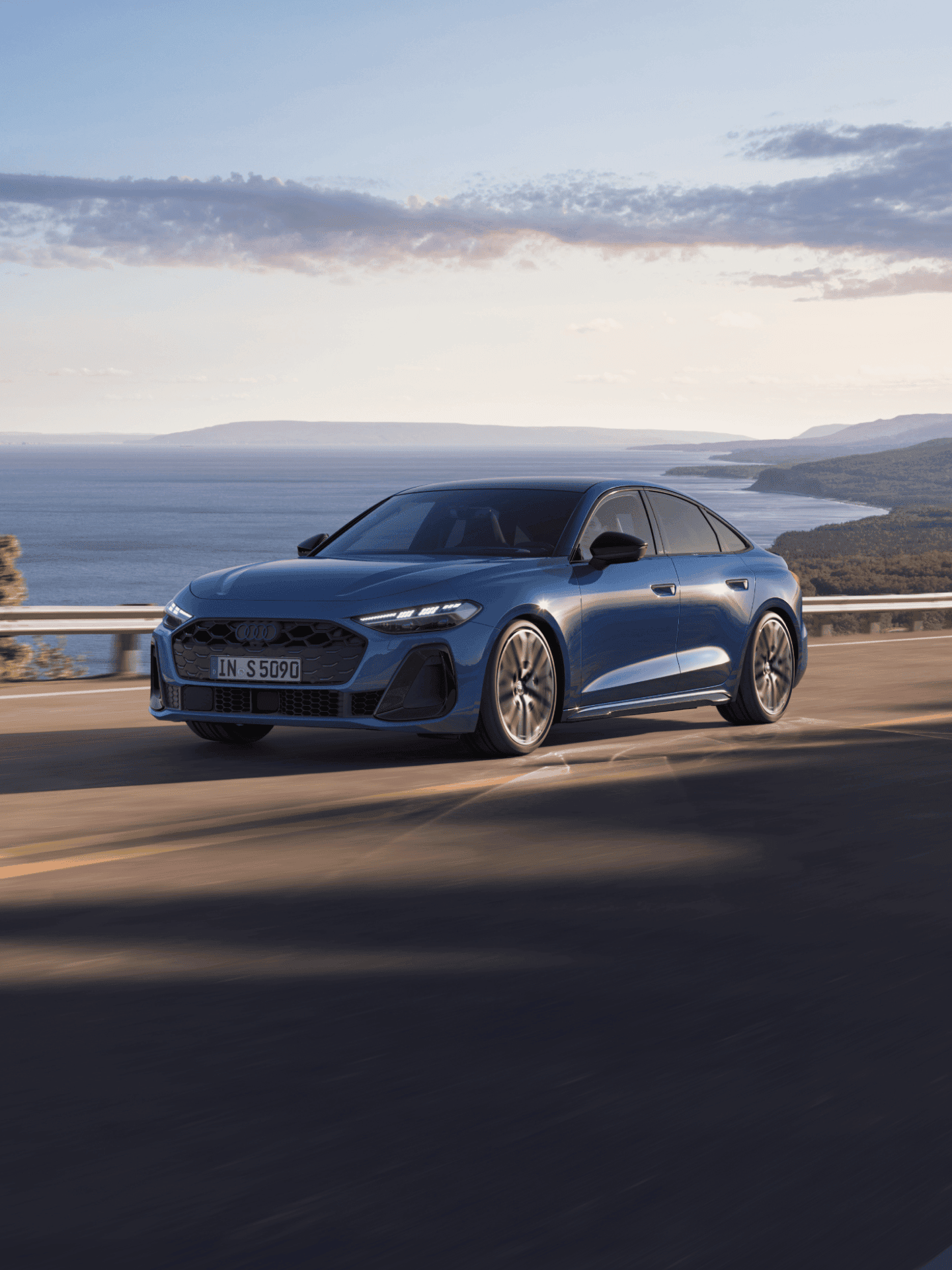 Blue Audi car driving on coastal road with sea and sky in background.