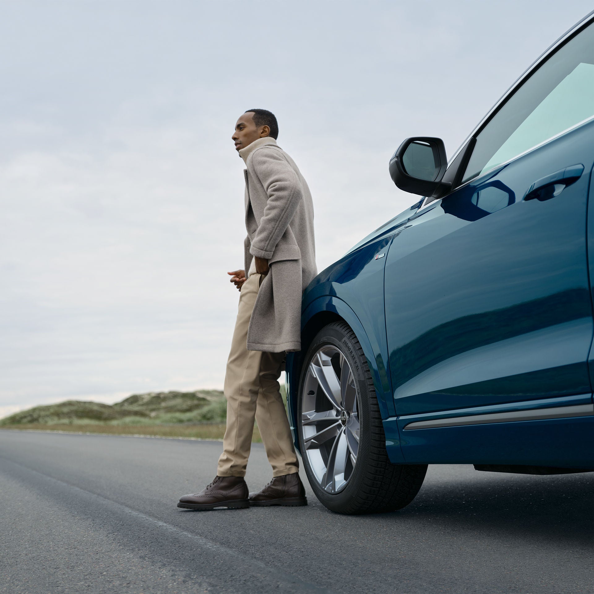  En man i profil som står och lutar sig mot en blå Audi Q8 på landsväg