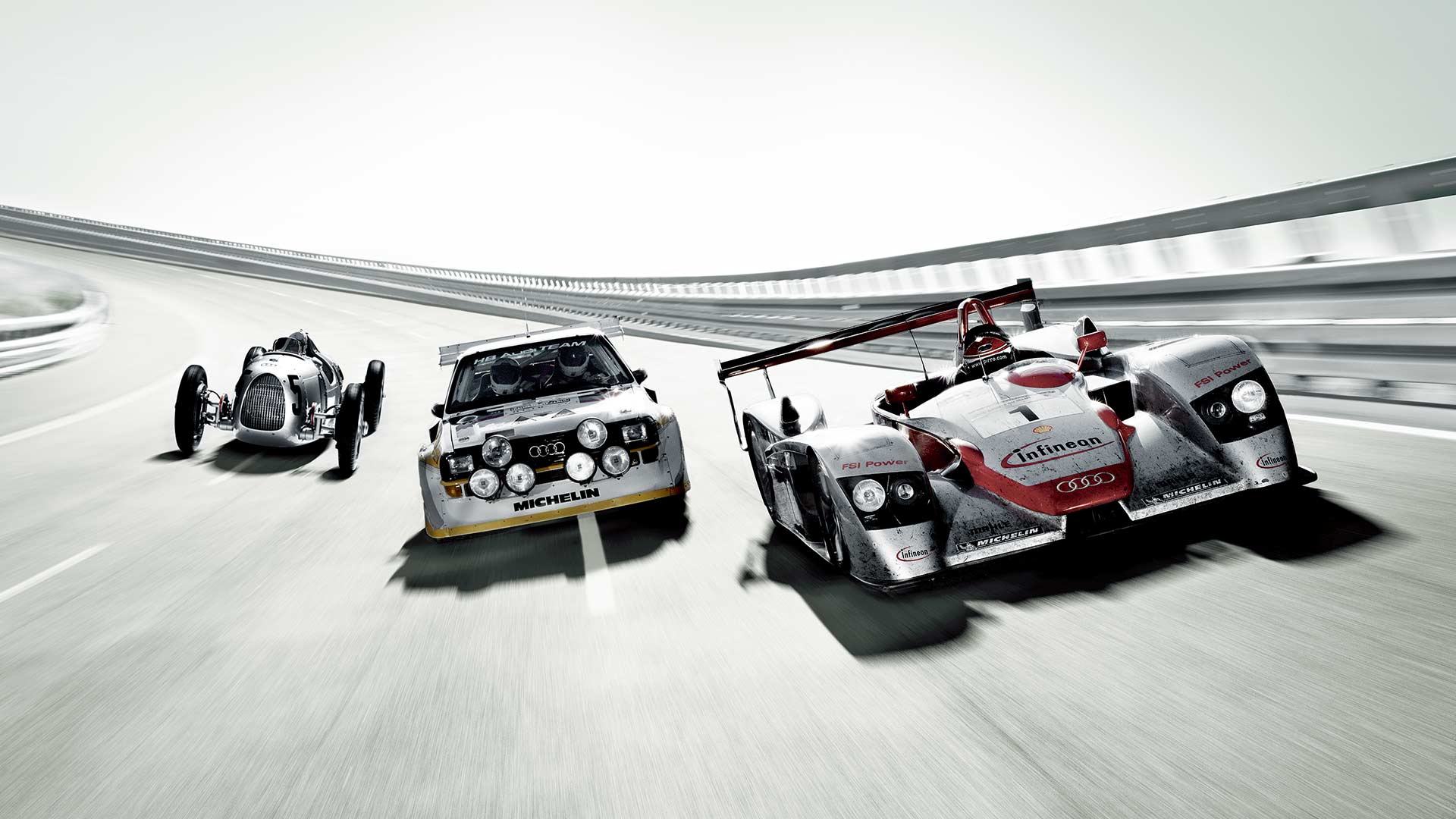 Tre Audi Sportbilar kör i en velodrom. Från vänster en Silverpil, i mitten en Audi quattro Brupp B och till höger en Audi LMP.