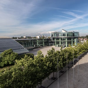Modernes Glasgebäude mit Innenhof, Bäumen und Solarpaneelen auf dem Dach, blauer Himmel im Hintergrund.