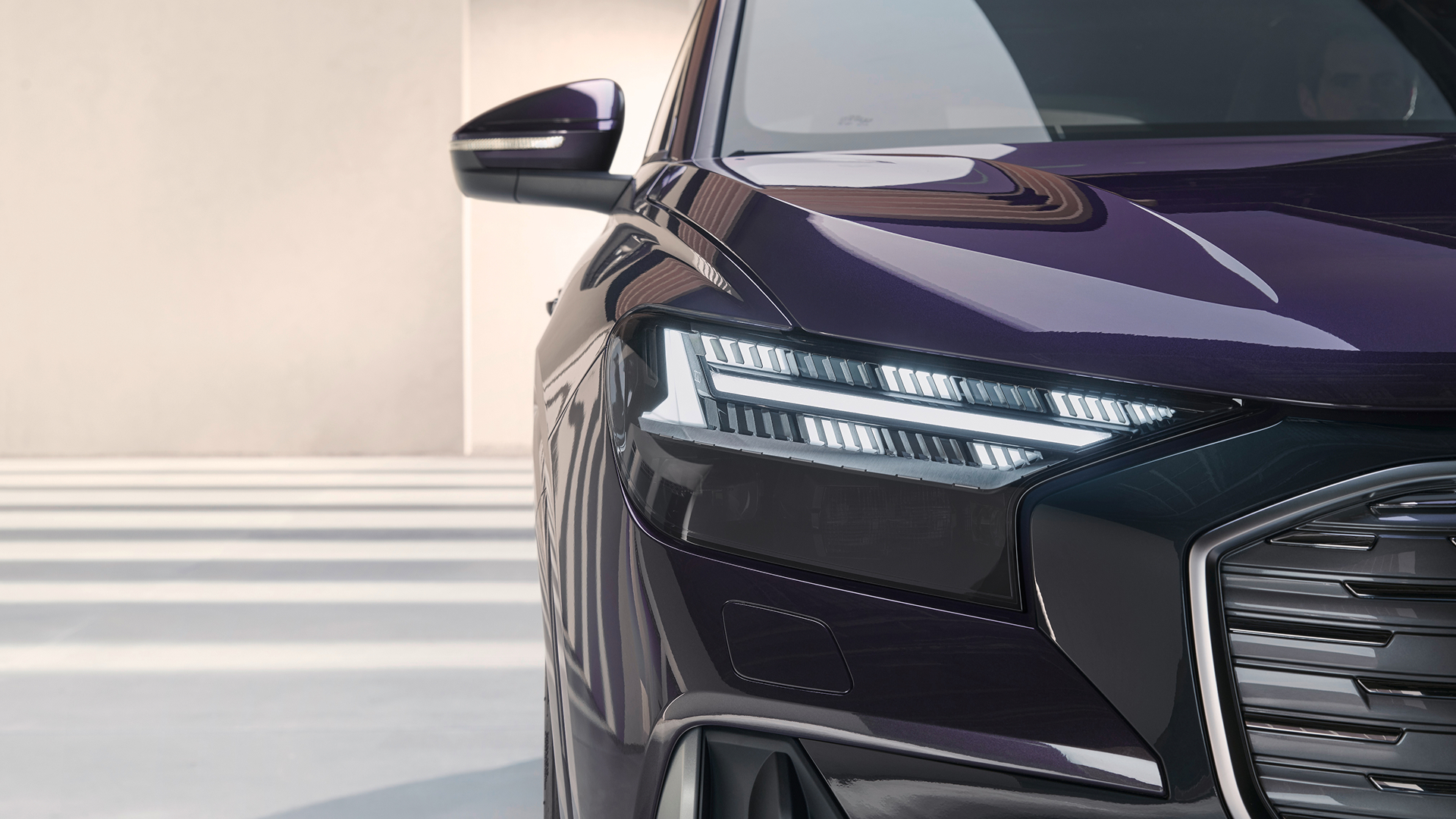 Dark purple Audi Q4 e-tron, close-up of front left headlight, grill and bonnet in well-lit room with white walls and floor.