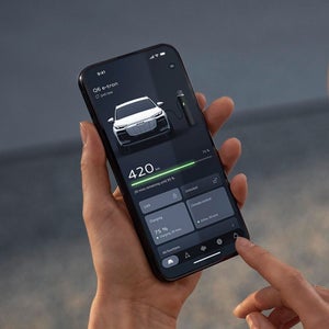 A person holds a smartphone displaying a car temperature control app next to a parked car. The setting is outdoors, creating a tech-savvy atmosphere.