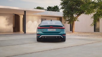 A teal Audi car parked in front of a modern house with a minimalist design.
