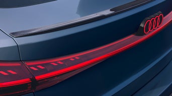  A grey audi vehicle driving on a coastal road with hills and the ocean in the background