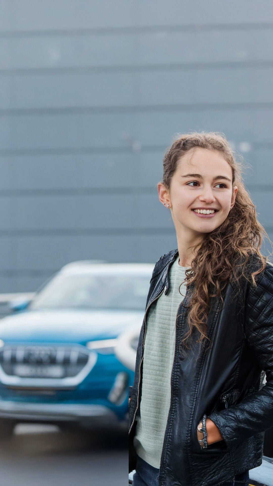 Junge Frau läuft auf einer Brücke und schaut lächelnd über ihre Schulter. Im Hintergrund fährt ein blauer Audi in ihre Richtung.