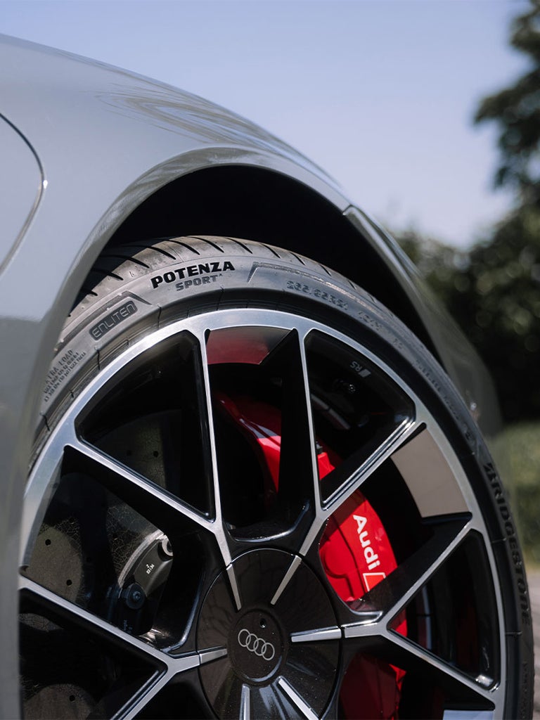 Nahaufnahme eines Audi-Rades mit schwarzer und silberner Felge, roter Bremssattel mit Audi-Logo und Bridgestone Potenza Sportreifen.