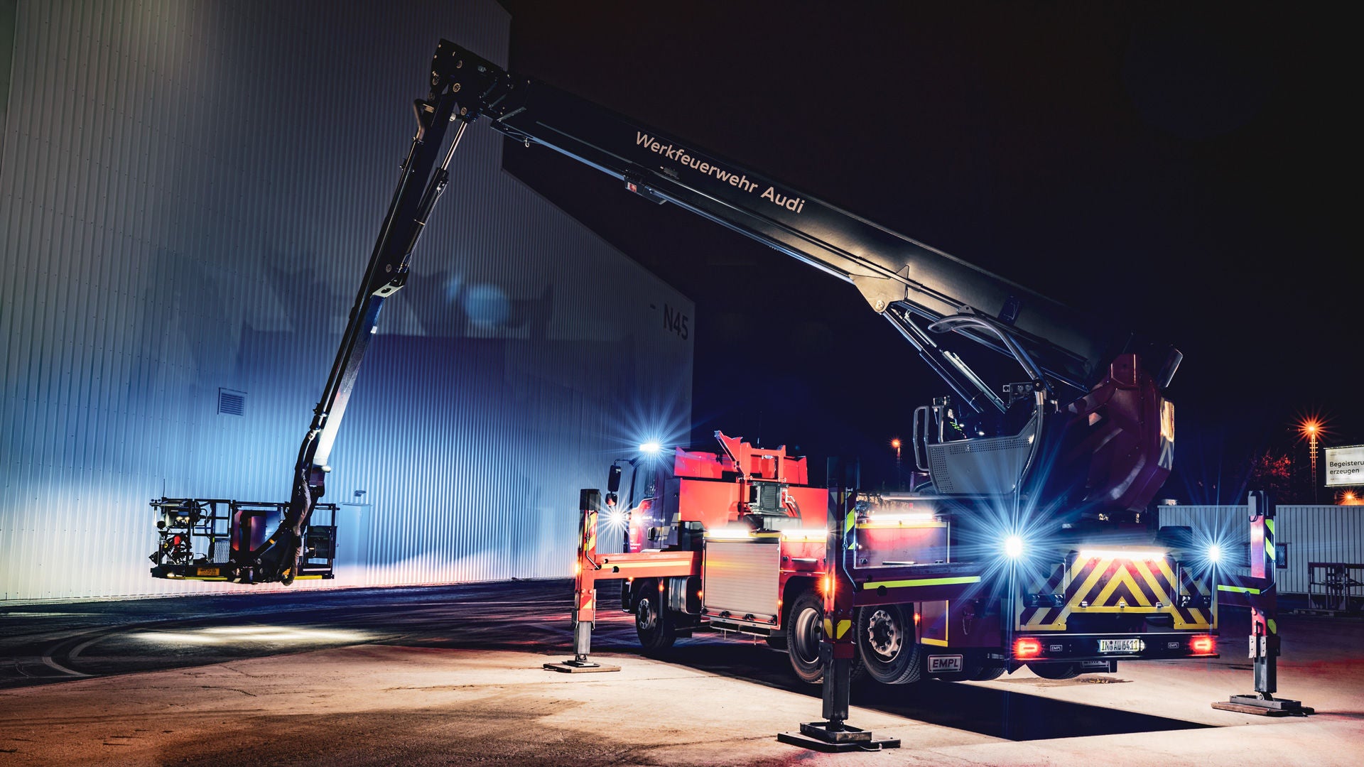 A fire truck with extended telescopic mast bears the inscription “Audi Fire Service” and illuminates a large production hall wall at night.