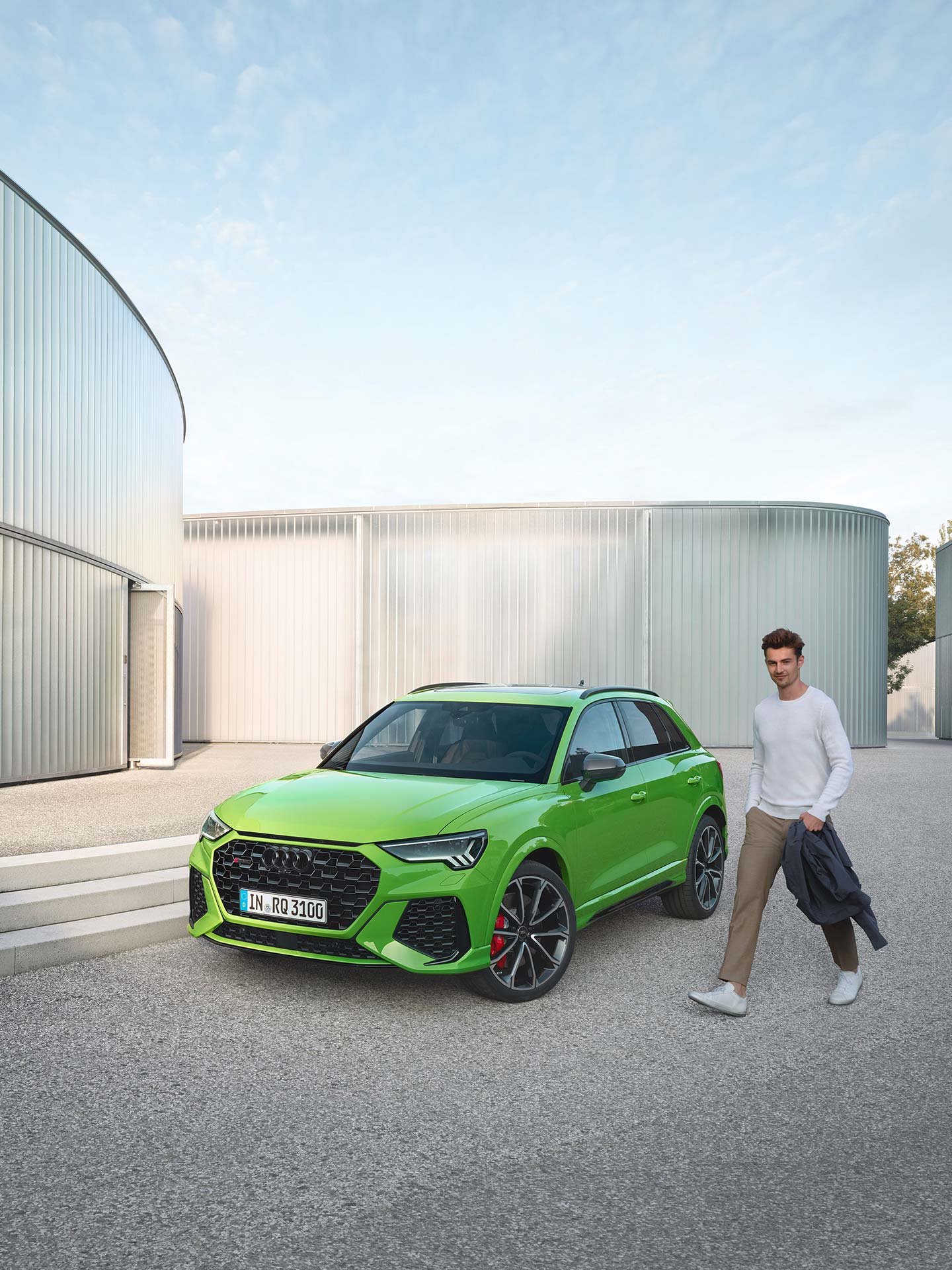 Man walking past green Audi RS Q3 parked outside a modern building.
