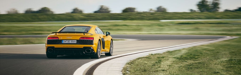Gelber Audi R8 Coupé fährt auf einer Rennstrecke (Rückansicht)
