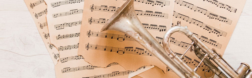 Alte Trompete liegt auf eingerissenen, vergilbten Notenblättern auf hellem Holztisch.
