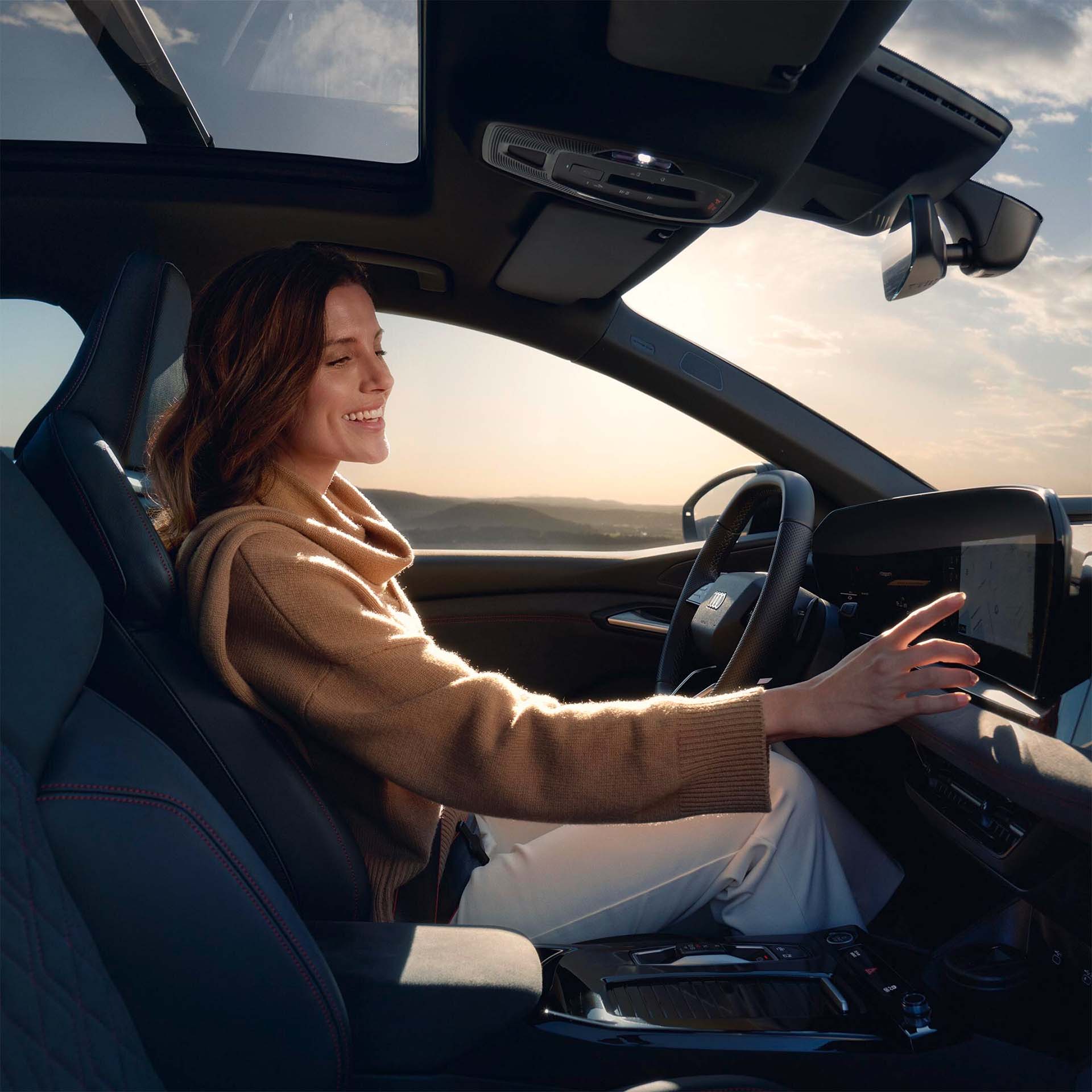 Kvinne sitter i førersete og trykker på MMI-skjermen