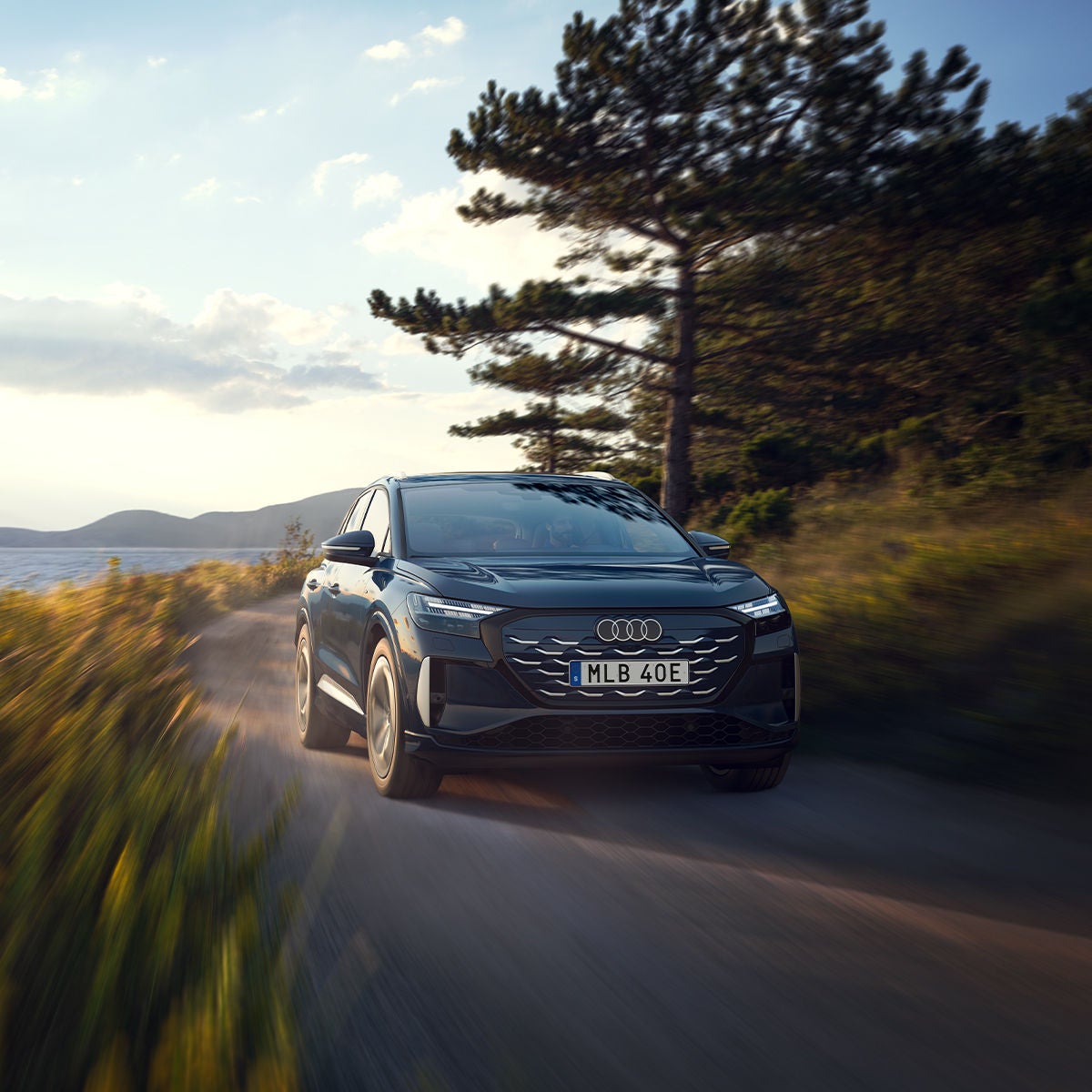 Audi Q4 e-tron kör på en landsväg i en naturnära omgivning med en sjö i bakgrunden.