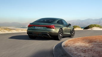 Ein grüner Audi RS e-tron GT performance fährt auf einer Küstenstraße mit Blick auf das Meer und Berge im Hintergrund.