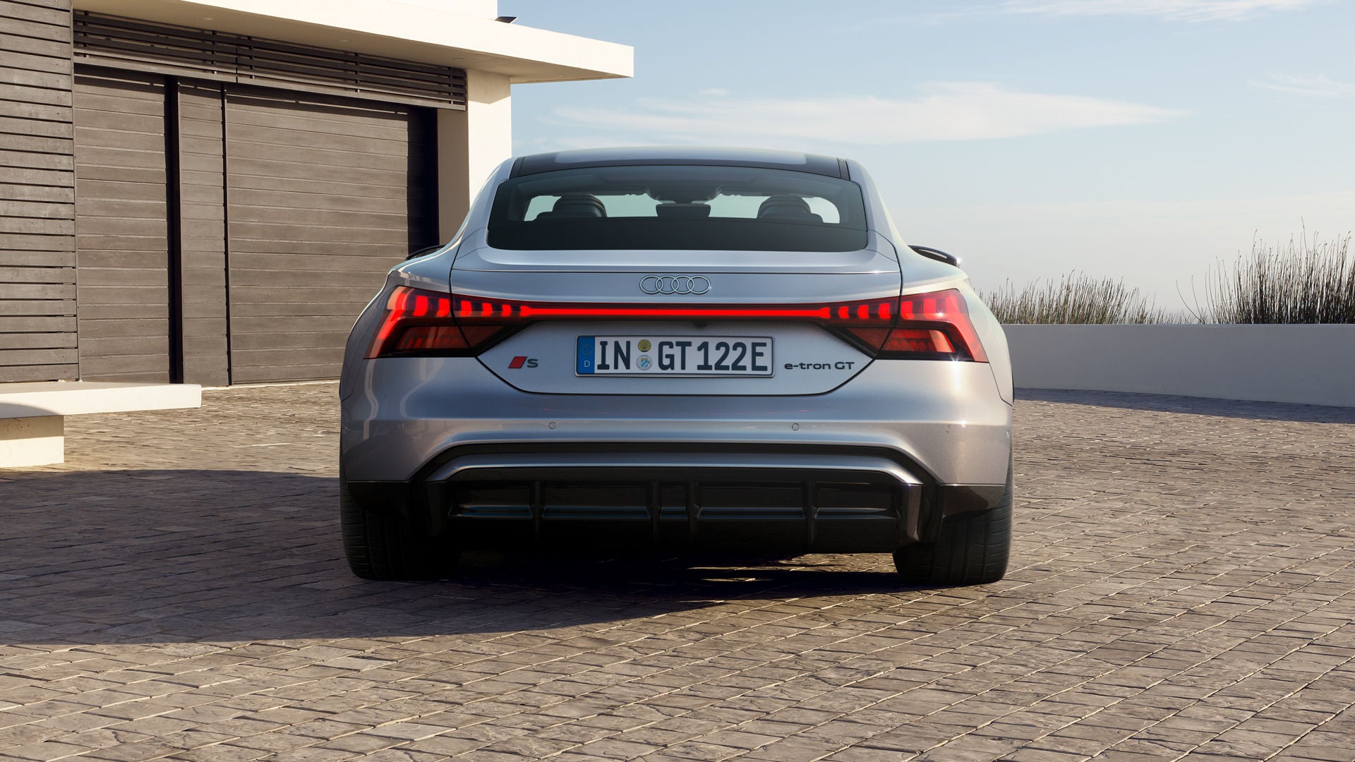 Die Heckansicht des Audi S e-tron GT auf einer gepflasterten Einfahrt. Die durchgehende LED-Lichtleiste und der sportliche Diffusor betonen das dynamische Design.