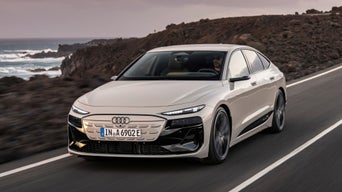 Audi A6 Sportback e-tron drives along a coastal road with rocky cliffs and ocean waves in the background, showcasing its sleek design.