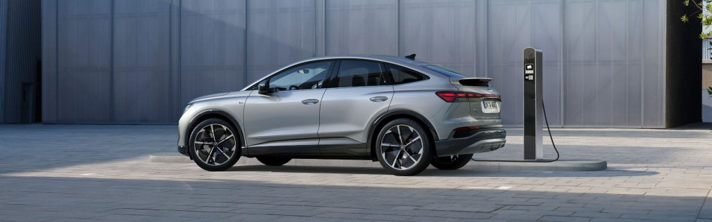 Silver electric SUV charging at a public charging station in a modern urban setting.