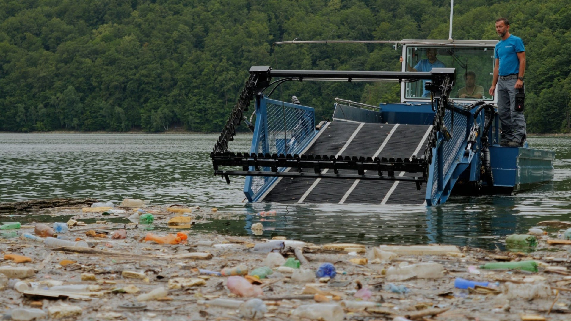 A man pushes rubbish together with a rubbish collection boat.