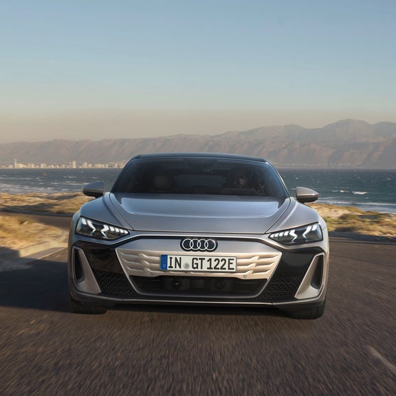 Die Frontansicht des Audi S e-tron GT auf einer kurvigen Küstenstraße. Die markanten LED-Scheinwerfer und das geschlossene, aerodynamische Kühlergrill-Design sind erkennbar.