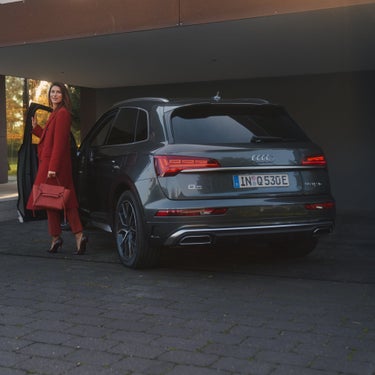 A person in a red coat carrying a matching bag walking towards Audi SUV.