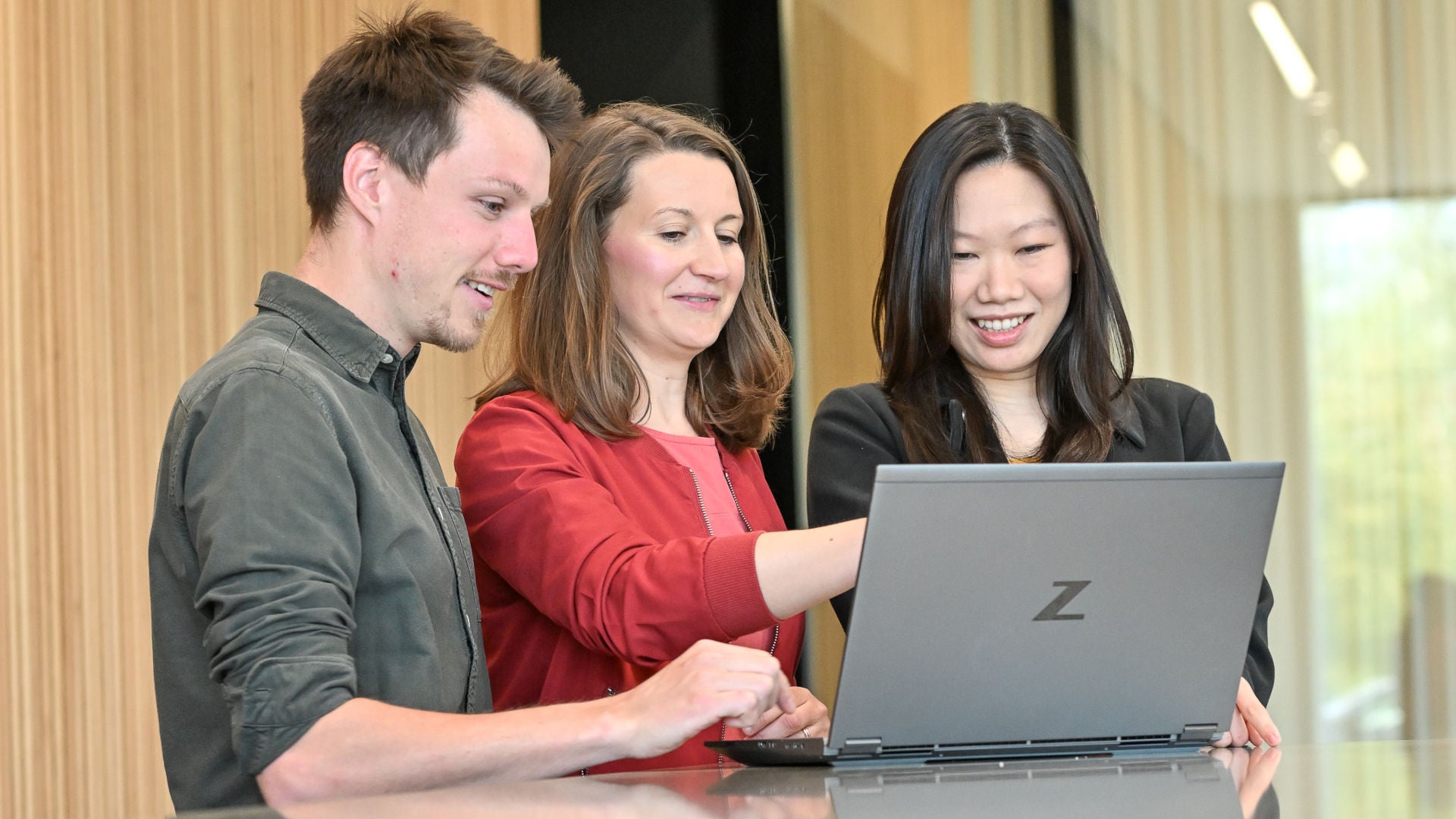 Drei Personen schauen gemeinsam auf einen Laptop in einem hellen Innenraum.