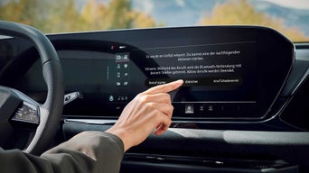 Blick aus dem Innenraum eines Audi auf eine Frau am Beifahrersitz und einen Mann draußen auf einer Küstenstraße.