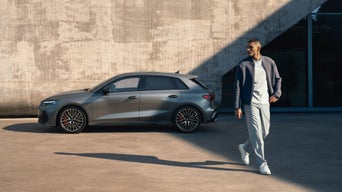 Ein Mann läuft vor einem grauen Audi, im Hintergrund eine Betonwand.