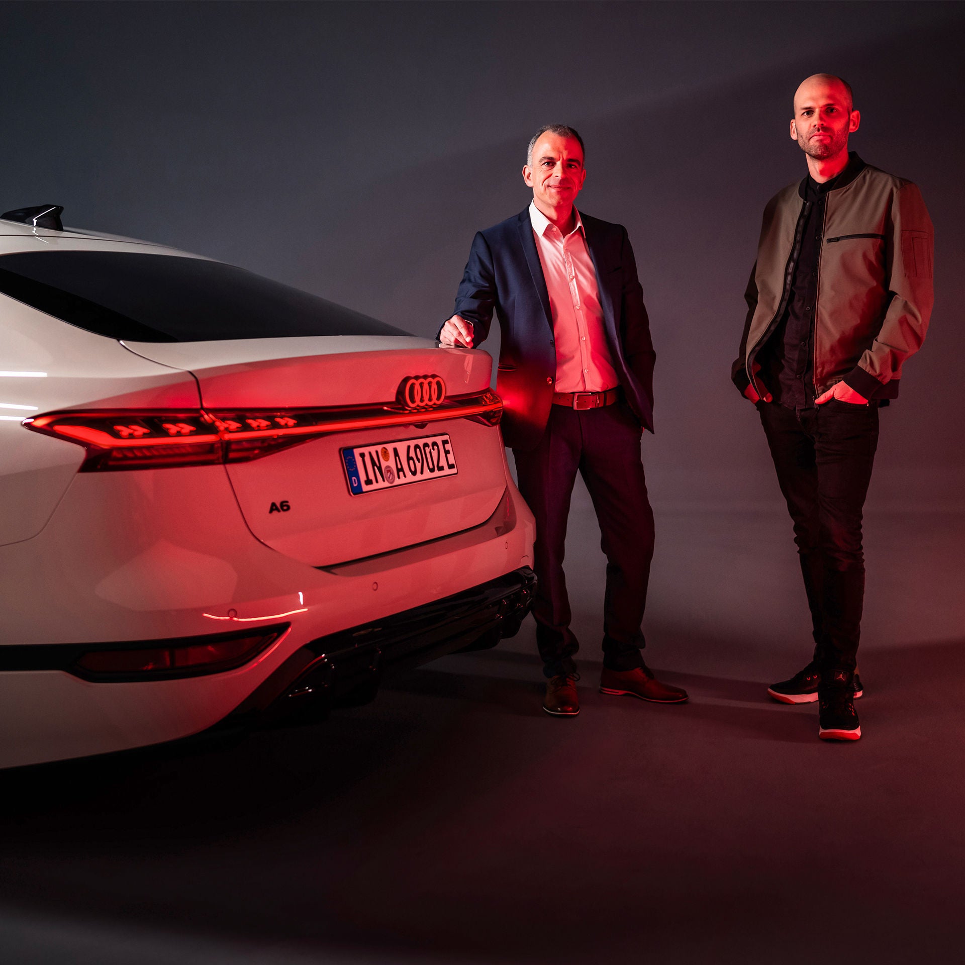 Stefan Staudacher and Christoph Häußinger illuminated in red by the rear lights of the Audi A6 Sportback e-tron.