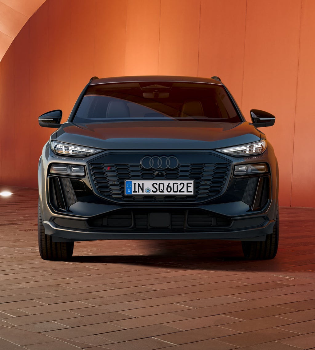 Frontprofil des SQ6 SUV e-tron, welcher vor einer orangenen, beleuchteten Wand steht.