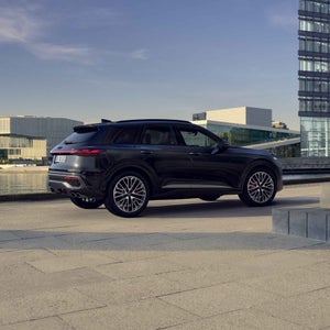 Die Edition One des SQ5 SUV mit Akzenten in mythosschwarz. Im Hintergrund befinden sich Gebäudefassaden aus Glas.