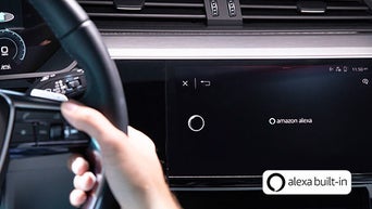 Hand am Lenkrad vor einem Display mit aktivierter Amazon Alexa-Sprachsteuerung im Audi-Cockpit.