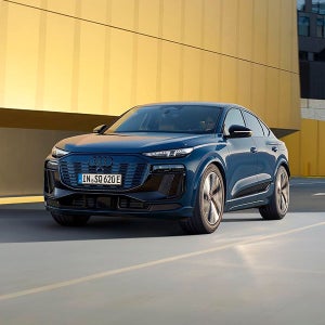 A blue Audi drives past a modern yellow building, exuding a sense of elegance and innovation under a clear sky, emphasising luxury and style.