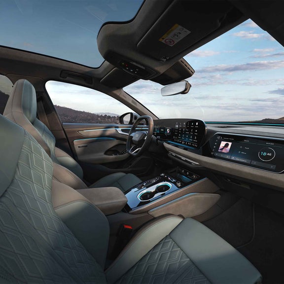 Innenraum eines Audi A6 Avant mit Sportsitzen, zwei großen Touchdisplays, Ambiente-Beleuchtung und Berglandschaft im Hintergrund.