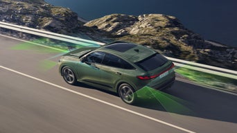 Vogelperspektive eines Audi Q5, der auf einer Schnellstraße an einer Küstenlandschaft vorbeifährt. Um den Q5 herum sind grafisch Sensoren angedeutet, die die Fahrerassistenzsysteme symbolisieren.