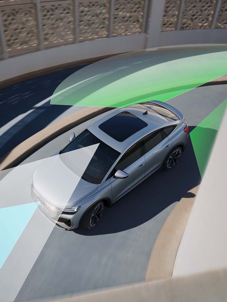 Silberner Audi Q4 Sportback e‐tron auf einer Straße mit farbigen Sensorfeldern zur Darstellung von Assistenzsystemen und Umfeldüberwachung.