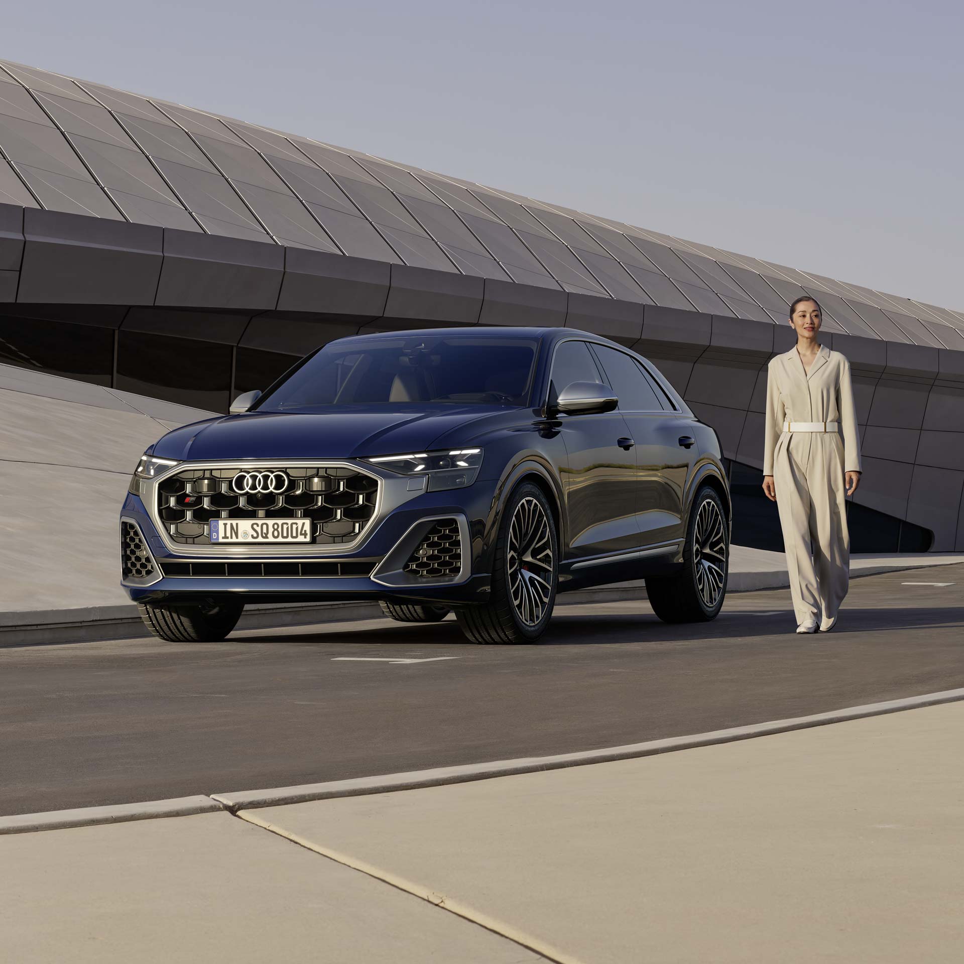 Eine Frau steht neben einem geparkten, dunkelblauen Audi SQ8 SUV vor einem modernen Gebäude.