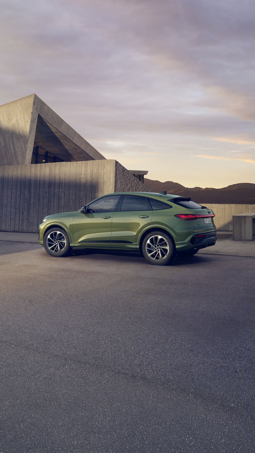 Ein grüner Q5 Sportback in Seitenansicht steht auf einem Parkplatz vor einem urbanen Haus in bergiger Umgebung.