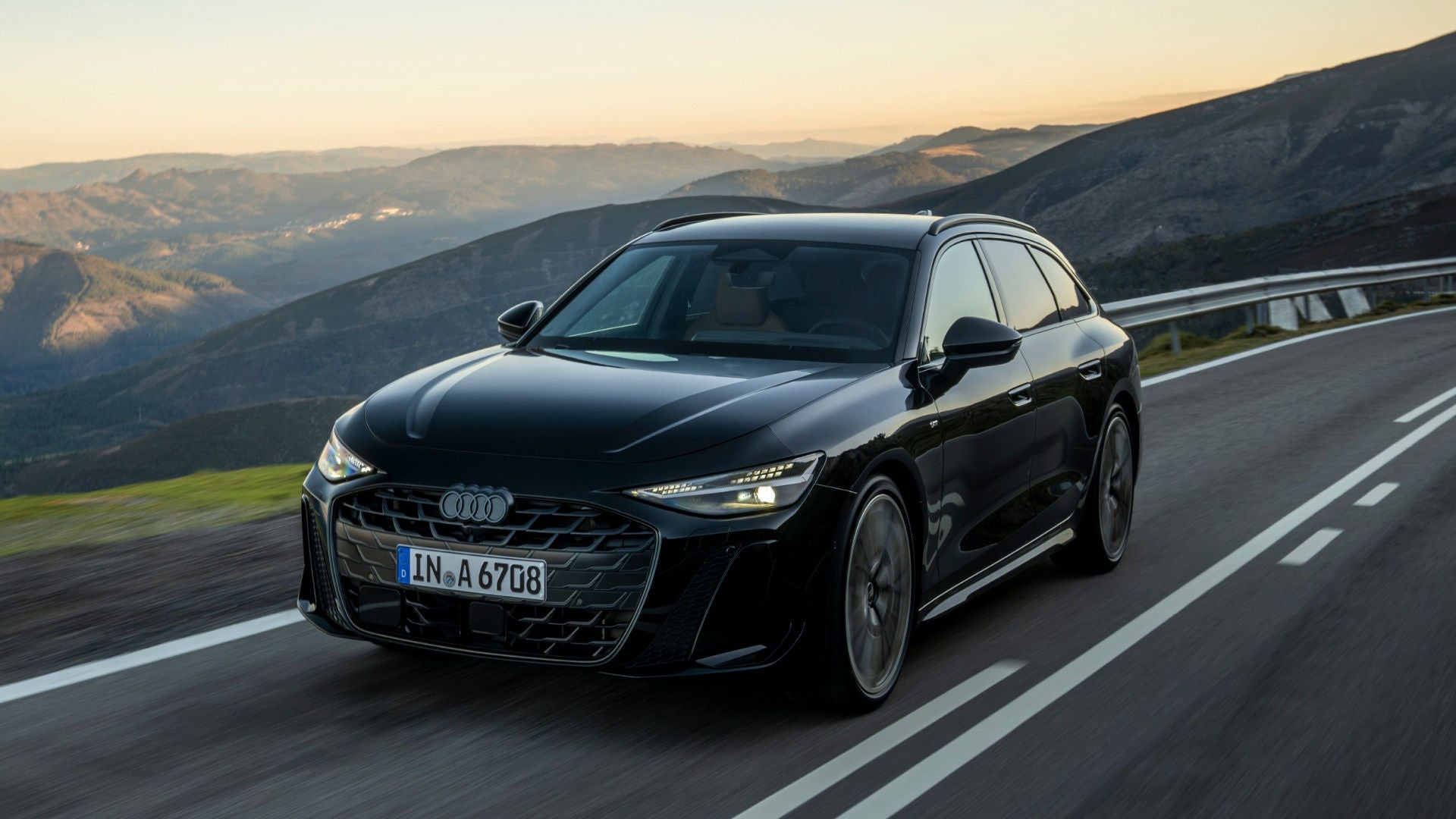 Ein Audi A6 Avant fährt durch eine Landschaft aus Bäumen und Hügeln. 