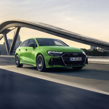 Grüner Audi RS 3 Sportback von vorn in Bewegung auf Brücke mit Stadt im Hintergrund.