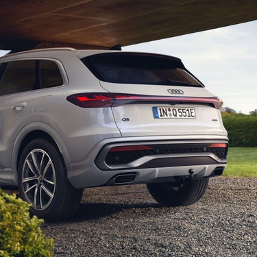 Audi Q5 SUV e-hybrid parked on gravel under a modern structure, showcasing its sleek rear design and distinctive taillights.