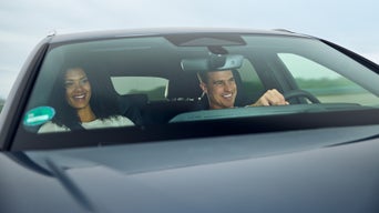 Frau und Mann lächeln während der Fahrt, Blick durch die Windschutzscheibe eines Autos.