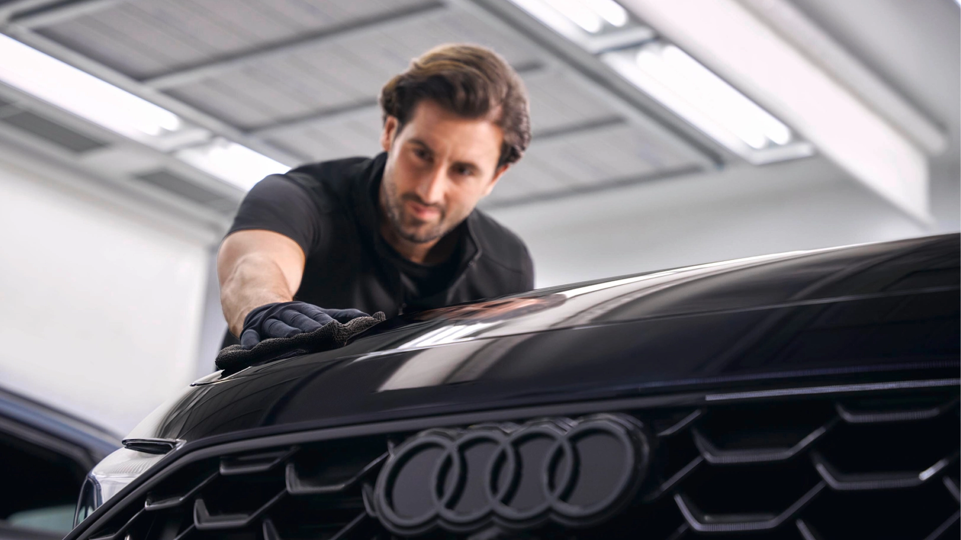 Technician polishing the front bonnet of an Audi vehicle in a workshop, with the Audi rings visible on the front grille.